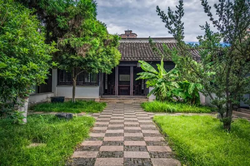 A serene garden featuring five round stone stools on a paved area, surrounded by lush greenery and trees under a clear sky.